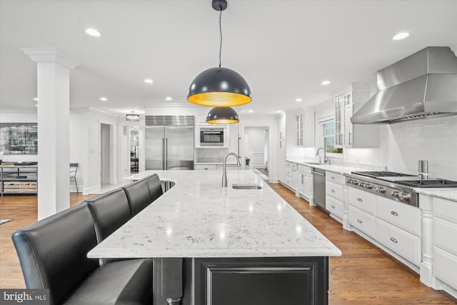 kitchen featuring wall chimney exhaust hood, wood-type flooring, sink, stainless steel appliances, and a large island