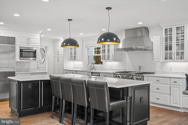 kitchen featuring appliances with stainless steel finishes, wall chimney range hood, white cabinets, and a center island with sink