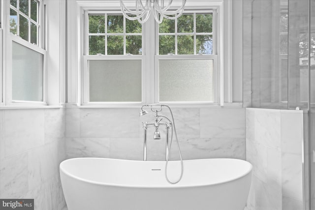 bathroom with a tub, tile walls, and a chandelier