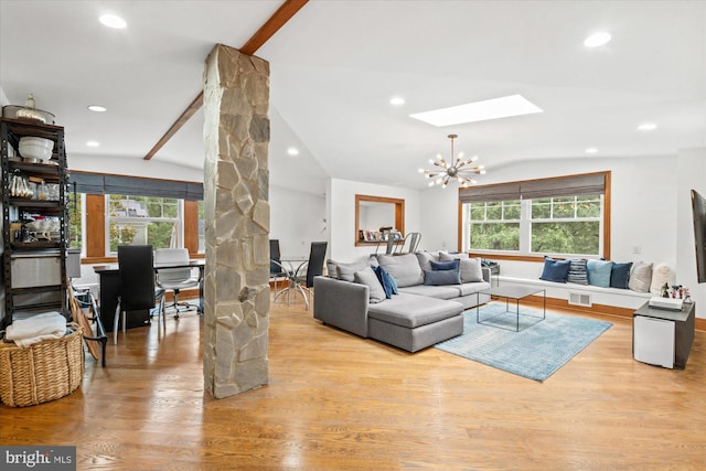 living room with light hardwood / wood-style floors, a healthy amount of sunlight, a chandelier, and vaulted ceiling with skylight