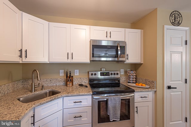 kitchen with stainless steel appliances, white cabinets, light stone counters, and sink