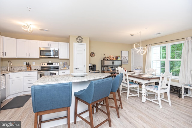 kitchen with light wood-type flooring, white cabinetry, appliances with stainless steel finishes, and light stone counters