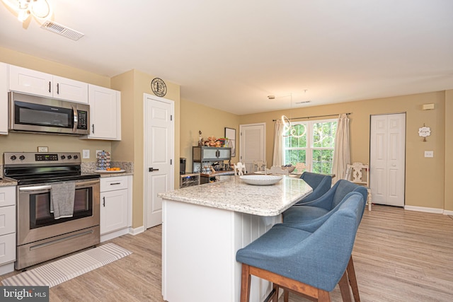 kitchen with hanging light fixtures, white cabinetry, stainless steel appliances, light wood-type flooring, and a center island