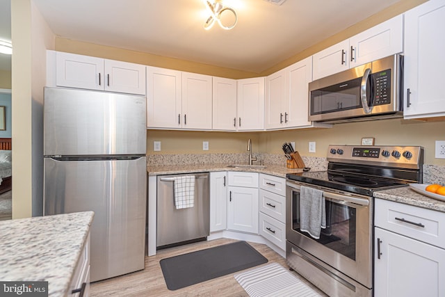 kitchen featuring sink, white cabinetry, light hardwood / wood-style flooring, appliances with stainless steel finishes, and light stone countertops