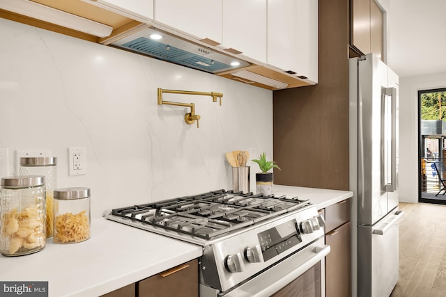 kitchen with dark brown cabinetry, ventilation hood, stainless steel appliances, light hardwood / wood-style flooring, and white cabinetry