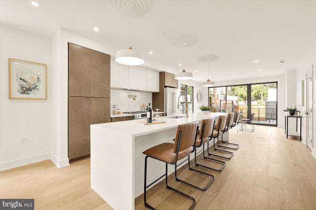 kitchen featuring a center island with sink, sink, decorative light fixtures, light hardwood / wood-style floors, and white cabinetry