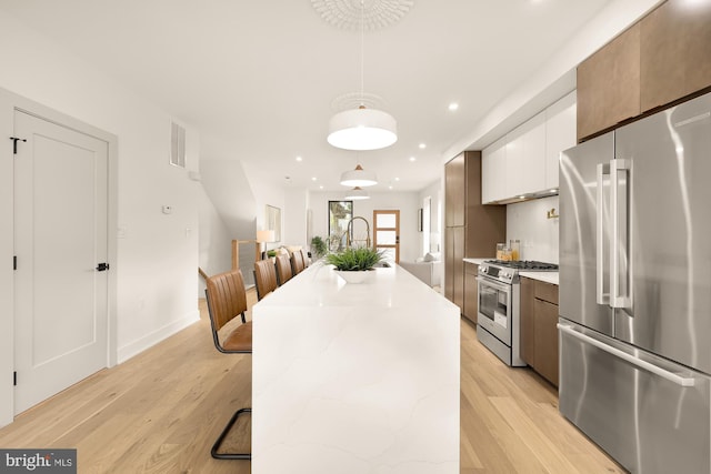 kitchen featuring a kitchen breakfast bar, light wood-type flooring, stainless steel appliances, white cabinetry, and hanging light fixtures