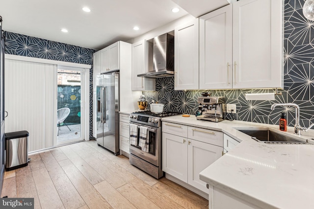 kitchen with stainless steel appliances, sink, light hardwood / wood-style floors, wall chimney range hood, and white cabinetry