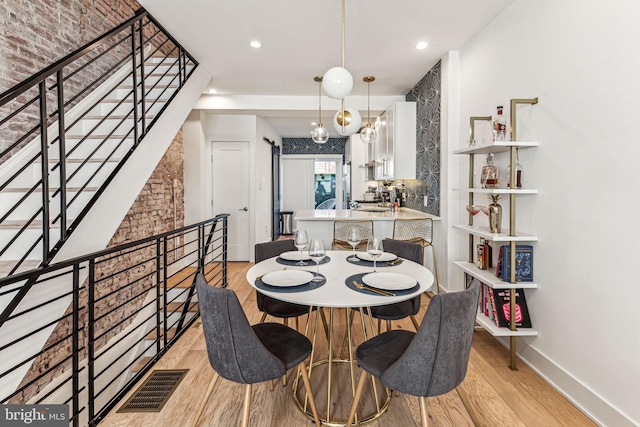 dining area featuring brick wall, an inviting chandelier, and light hardwood / wood-style flooring