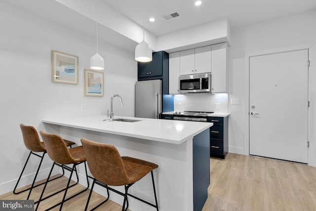 kitchen featuring white cabinets, sink, decorative light fixtures, stainless steel appliances, and a kitchen bar