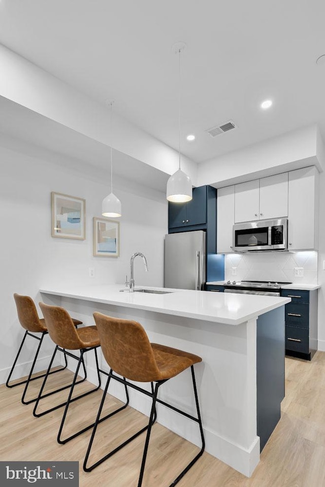 kitchen featuring appliances with stainless steel finishes, a breakfast bar, pendant lighting, light hardwood / wood-style flooring, and sink