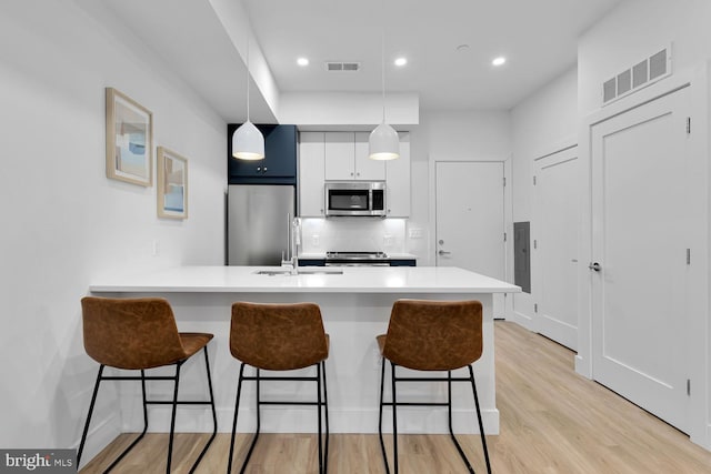 kitchen featuring appliances with stainless steel finishes, white cabinetry, light wood-type flooring, a kitchen bar, and decorative light fixtures