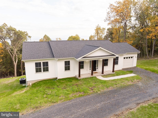 view of front of property with central air condition unit, a garage, a porch, and a front lawn