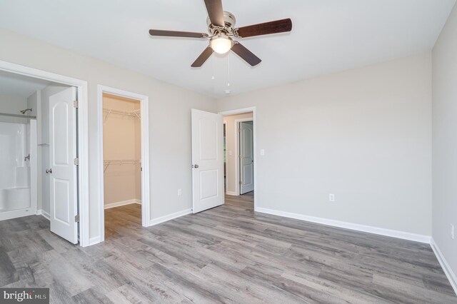 unfurnished bedroom featuring a spacious closet, a closet, light wood-type flooring, and ceiling fan