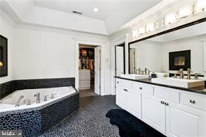 bathroom featuring vanity, a relaxing tiled tub, and a tray ceiling