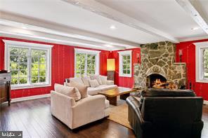 living room with beam ceiling, plenty of natural light, dark wood-type flooring, and a stone fireplace