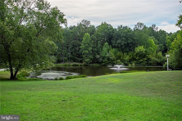 surrounding community featuring a water view, a wooded view, and a lawn