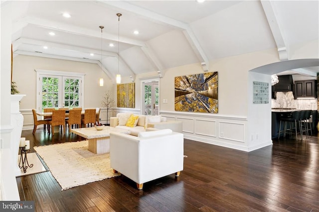 living room with a decorative wall, lofted ceiling with beams, dark wood-type flooring, arched walkways, and a wainscoted wall