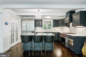 kitchen with beamed ceiling, wall chimney exhaust hood, stainless steel stove, dark hardwood / wood-style floors, and a center island