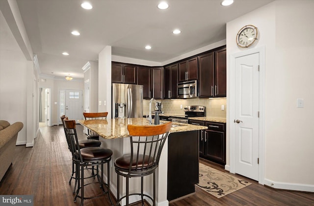 kitchen with stainless steel appliances, a breakfast bar, light stone counters, an island with sink, and dark wood-type flooring