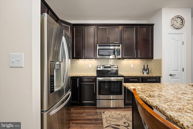 kitchen with dark brown cabinetry, appliances with stainless steel finishes, dark hardwood / wood-style floors, and light stone countertops