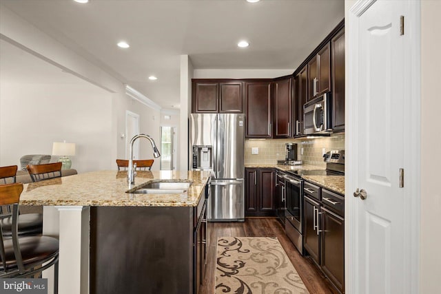 kitchen featuring light stone counters, appliances with stainless steel finishes, sink, an island with sink, and dark wood-type flooring