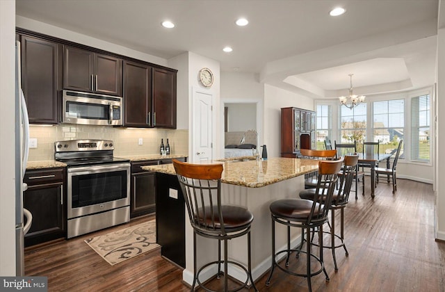 kitchen featuring dark hardwood / wood-style flooring, sink, an island with sink, appliances with stainless steel finishes, and decorative light fixtures