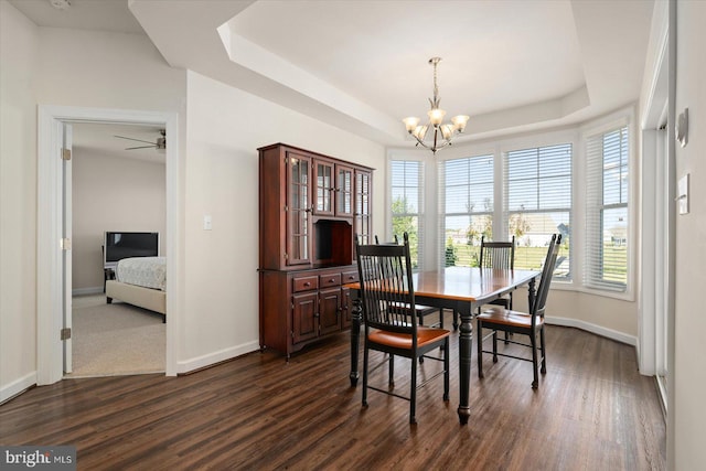 dining room with dark wood-type flooring, ceiling fan with notable chandelier, and a raised ceiling