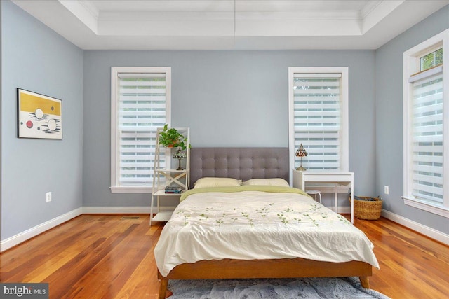 bedroom with ornamental molding, a raised ceiling, and hardwood / wood-style floors