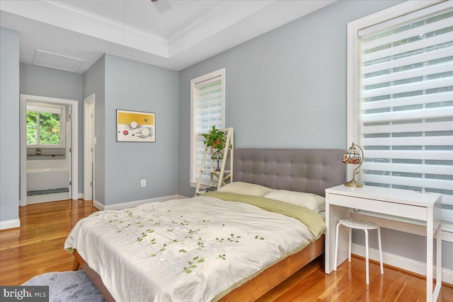 bedroom featuring ornamental molding, wood-type flooring, a tray ceiling, and connected bathroom