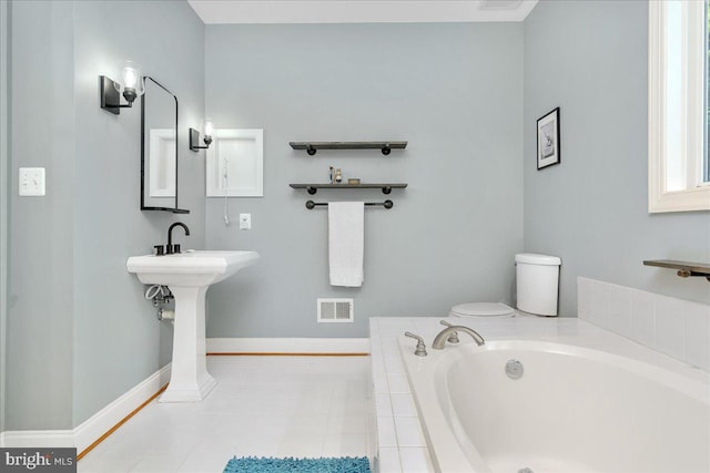 bathroom with tiled tub, tile patterned floors, and toilet