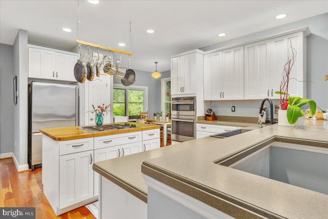 kitchen featuring white cabinets, light wood-type flooring, stainless steel appliances, and hanging light fixtures