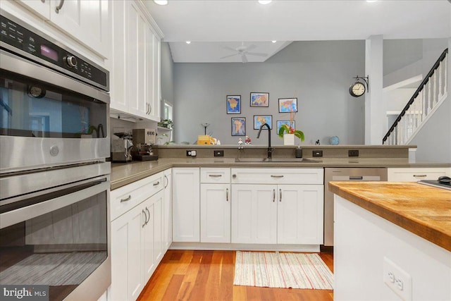 kitchen with white cabinets, sink, kitchen peninsula, appliances with stainless steel finishes, and light wood-type flooring