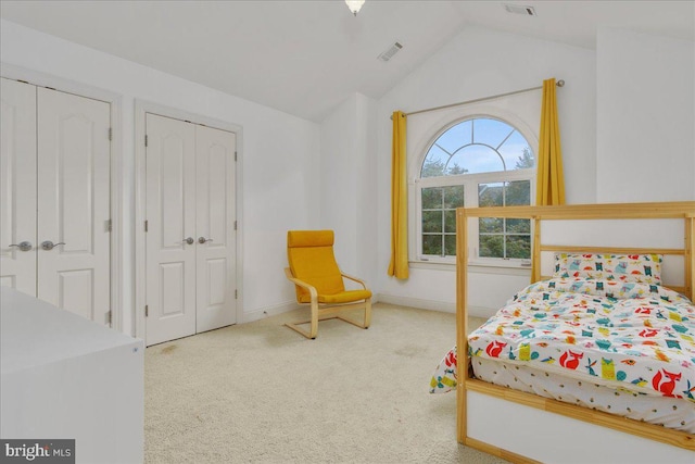 carpeted bedroom featuring two closets and vaulted ceiling