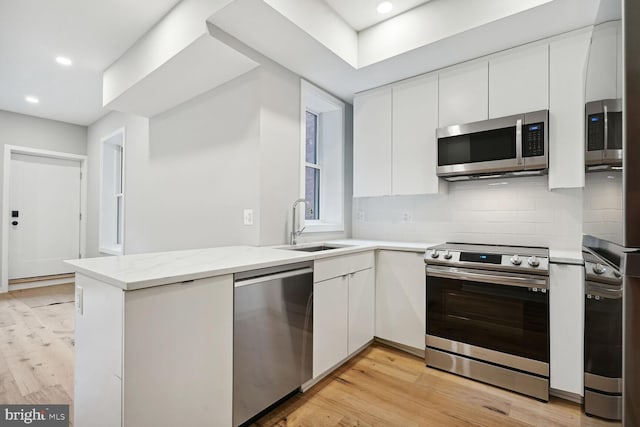 kitchen with light hardwood / wood-style floors, appliances with stainless steel finishes, backsplash, white cabinets, and sink