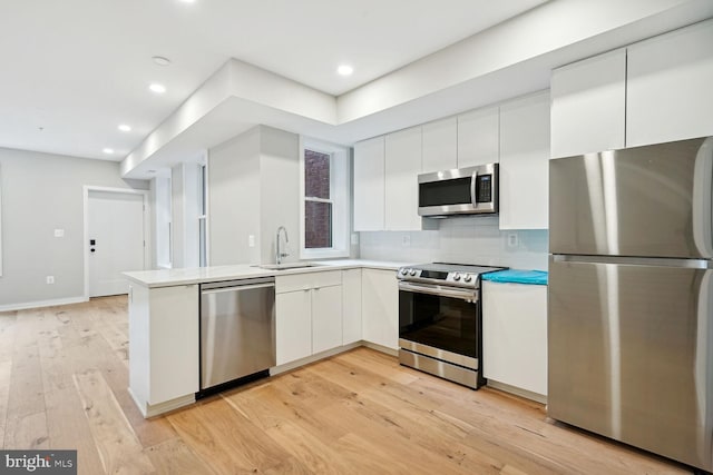 kitchen featuring appliances with stainless steel finishes, decorative backsplash, light wood-type flooring, white cabinets, and sink