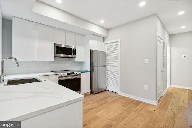 kitchen featuring backsplash, sink, white cabinetry, appliances with stainless steel finishes, and light stone counters