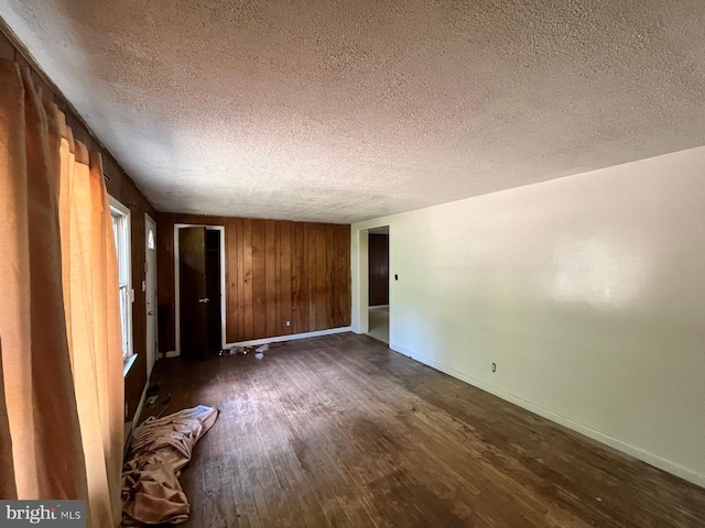 unfurnished room with wooden walls, a textured ceiling, and dark hardwood / wood-style floors