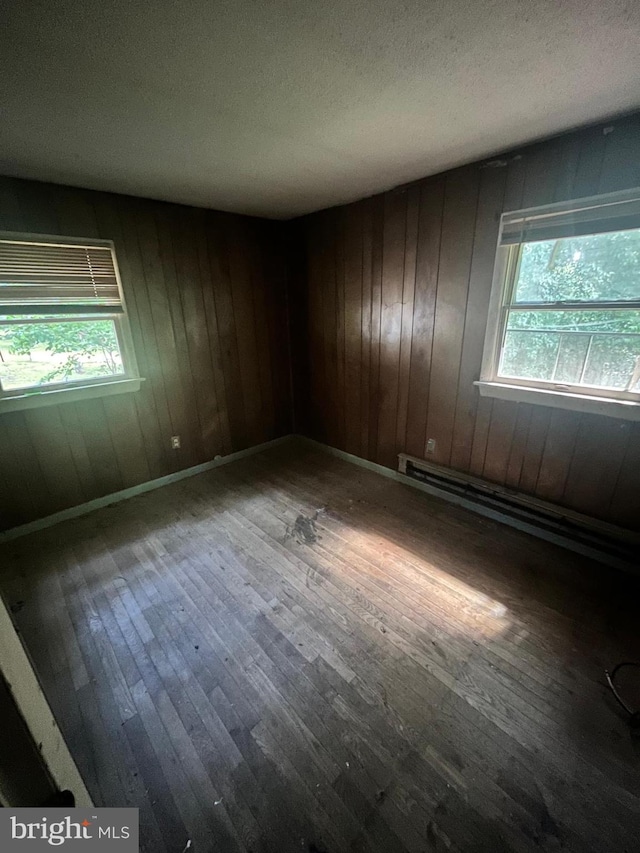 unfurnished room featuring baseboard heating, a textured ceiling, wood walls, and hardwood / wood-style floors