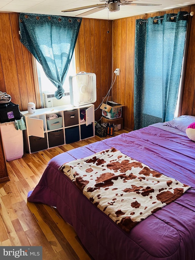 bedroom with wood walls, wood-type flooring, and ceiling fan