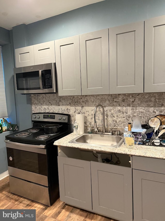 kitchen with light hardwood / wood-style flooring, gray cabinets, appliances with stainless steel finishes, and sink