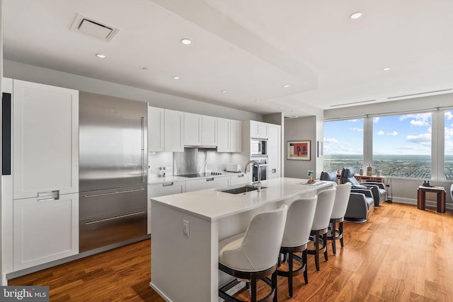 kitchen featuring light hardwood / wood-style floors, white cabinetry, stainless steel microwave, a kitchen island with sink, and sink