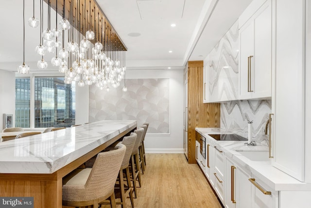 kitchen with light hardwood / wood-style flooring, white cabinetry, hanging light fixtures, and light stone countertops