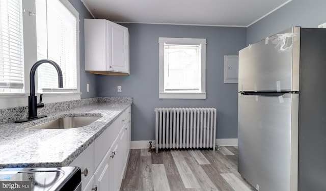 kitchen with radiator, sink, stainless steel fridge, white cabinetry, and light stone countertops