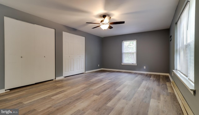 unfurnished bedroom with multiple closets, ceiling fan, and light hardwood / wood-style flooring