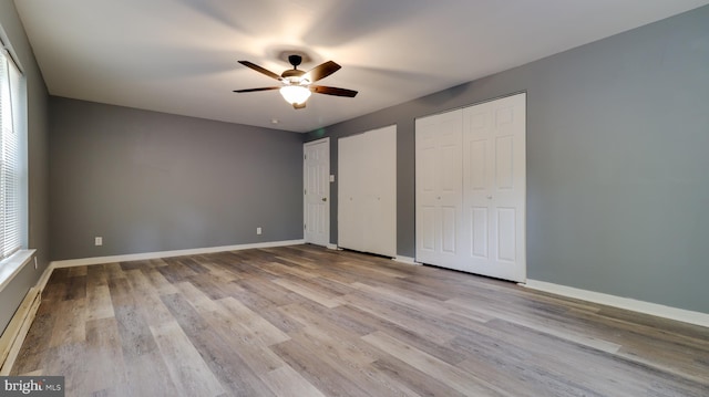 unfurnished bedroom featuring multiple closets, ceiling fan, a baseboard heating unit, and light wood-type flooring