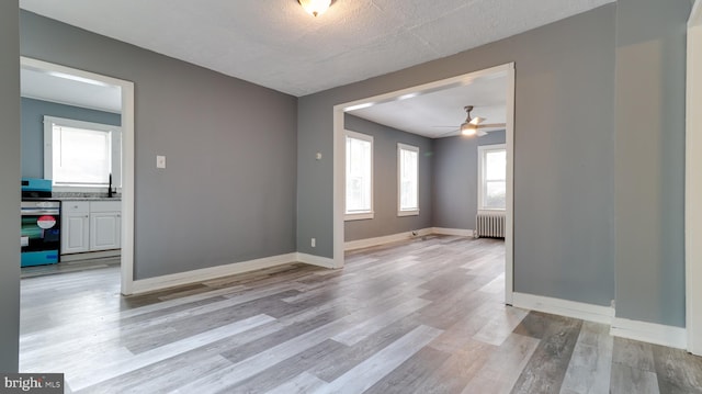 empty room featuring radiator, sink, ceiling fan, a textured ceiling, and light wood-type flooring