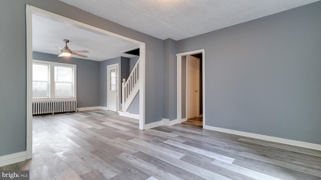 spare room with ceiling fan, radiator heating unit, light hardwood / wood-style floors, and a textured ceiling