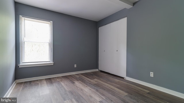 interior space featuring multiple windows, hardwood / wood-style flooring, beam ceiling, and a closet