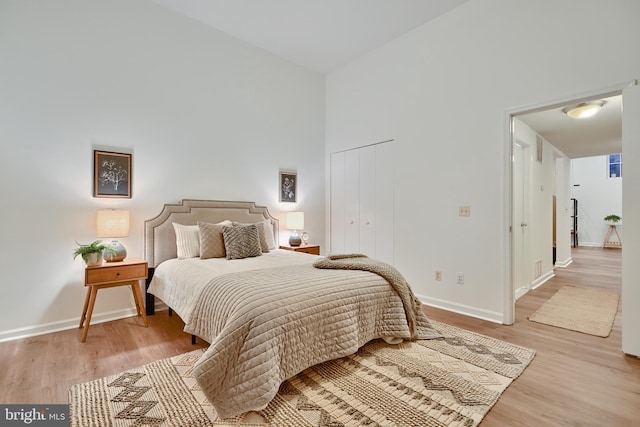 bedroom with a closet, light wood-type flooring, and a high ceiling